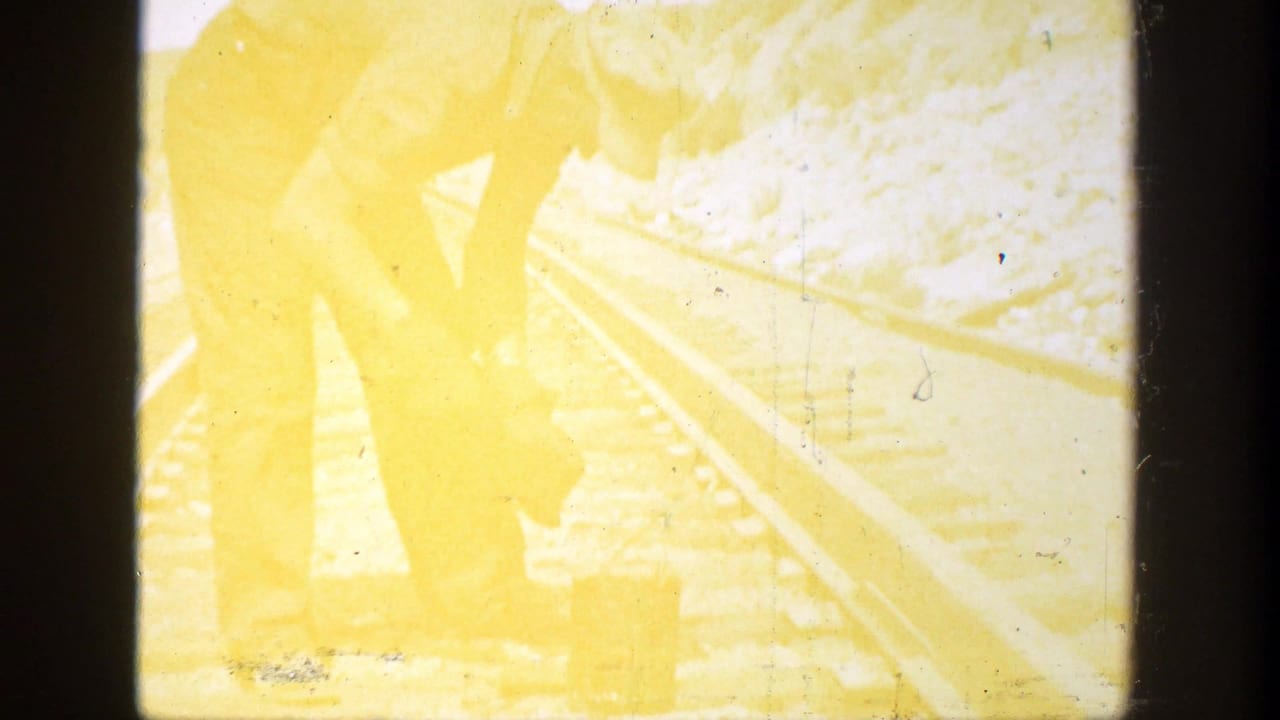 Yellow-tinted frame of a worker bent over railroad tracks.