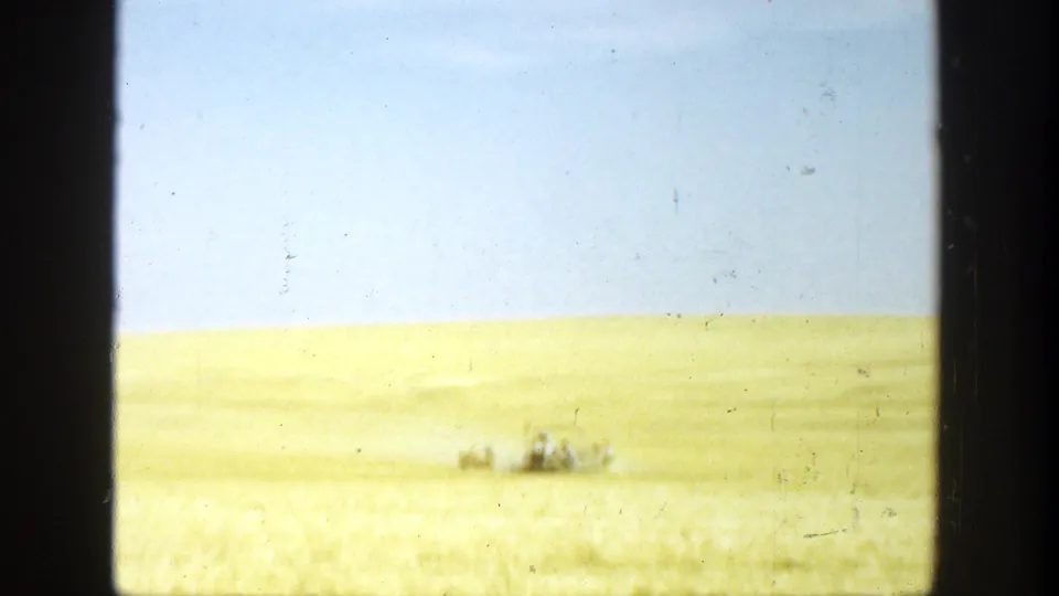The home-movie view holds on a broad sunlit field with a small tractor or vehicle moving in the distance.