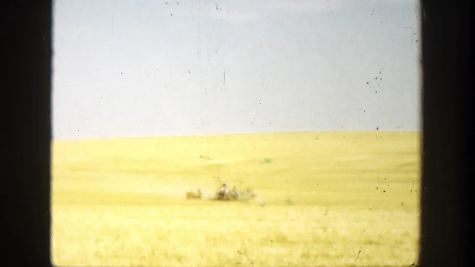1936 California rural field frame showing distant clustered people under a clear sky, with dust and heavy film-frame borders.