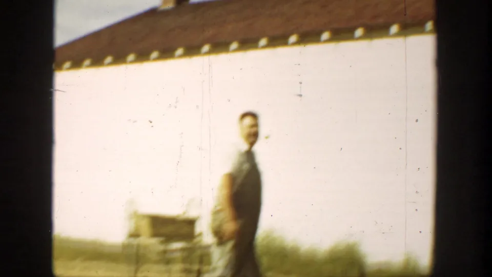 1936 California home-movie frame showing an adult man near a white farm building, with wagon-like equipment in the foreground.