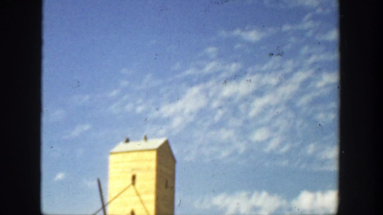 Yellow tower-like building below a blue sky with small white clouds.