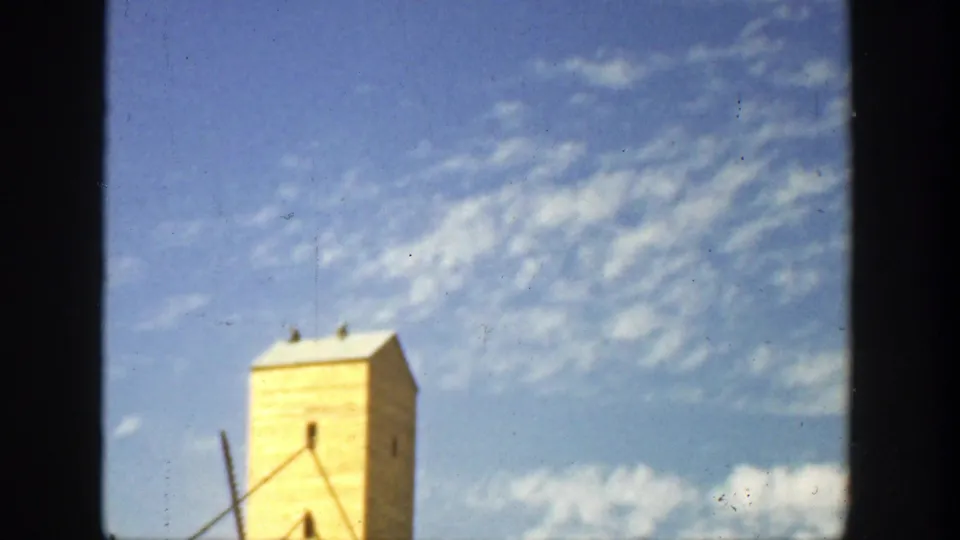 A sunlit yellow building top appears within dark 8mm frame borders, set against blue sky and fluffy white clouds.