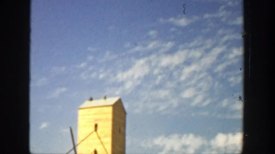 Soft-focused 8mm frame of a yellow tower-like structure under a bright blue sky with scattered cloud texture.