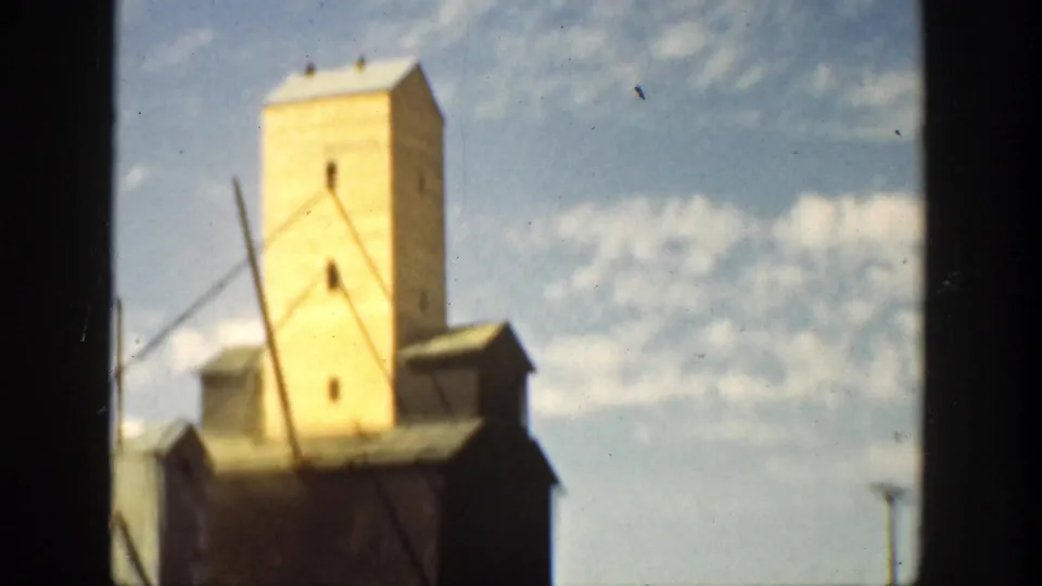 1936 California home-movie frame showing more of the yellow tower, roof edges, and diagonal lines beneath a clouded blue sky.