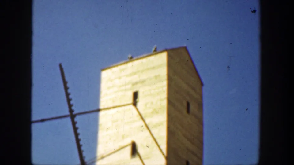 1936 8mm view of a tall pale tower with small dark openings, diagonal foreground structure, and strong blue sky.