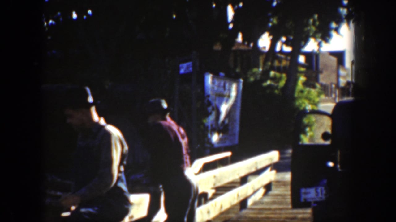 Two men stand or work near a wooden bridge or platform in partial shade.