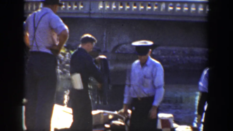 1936 California frame showing workers in hats and suspenders near a low riverside wall and equipment in bright sun.