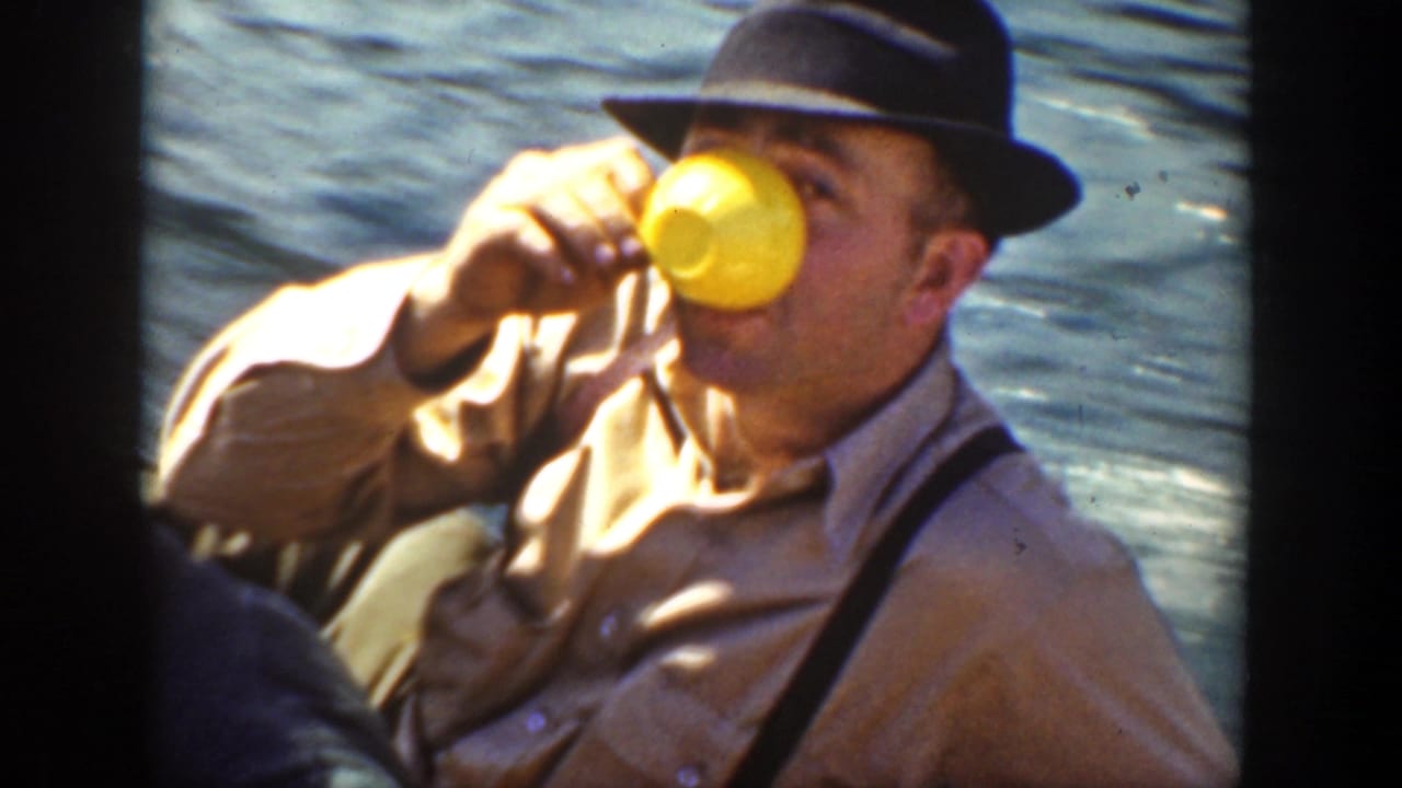 In 1936 California home-movie footage, a man in a fedora and suspenders drinks from a yellow cup beside rippling river water.