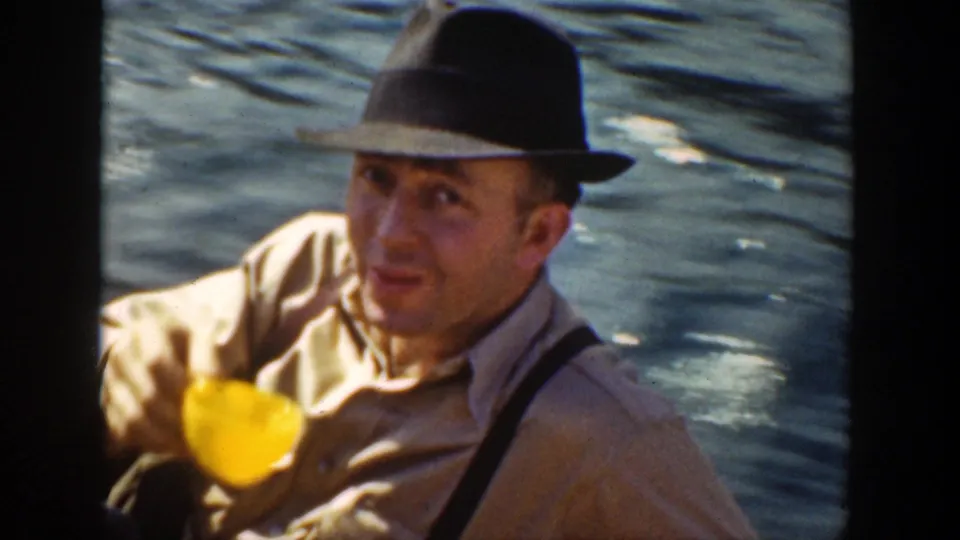 A man in a fedora and suspenders holds a yellow cup and looks toward the camera during a 1936 California river outing.