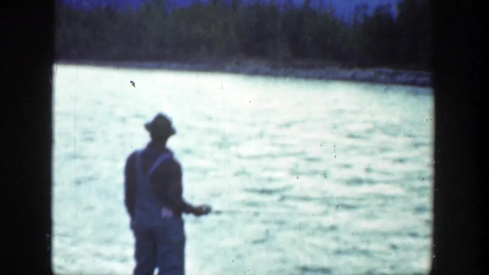 A man in a hat stands near bright river water, appearing to handle fishing line in 1936 California home-movie footage.