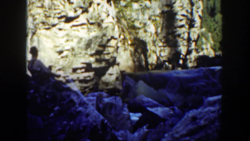 The seated man appears at the left edge of the 1936 California waterfall scene, partly silhouetted against pale rock and moving water.