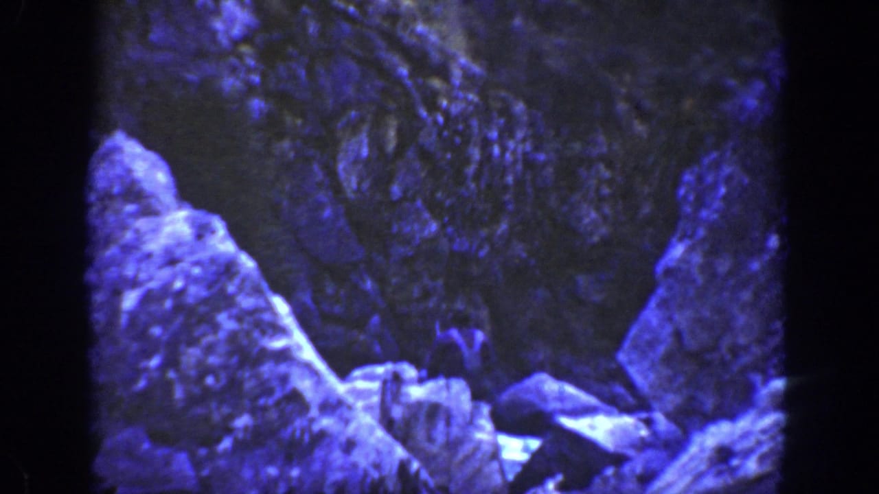 Blue-tinted rocky canyon scene with large stone formations and dark film borders.