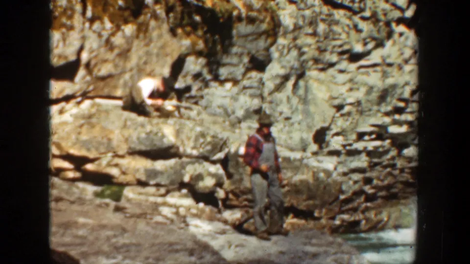 1936 California canyon frame showing one man standing near water while another sits on a higher rock ledge.