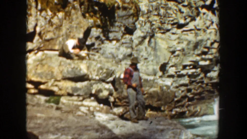 1936 California home-movie still of two men in a rocky river canyon, one seated on a ledge and one standing below.