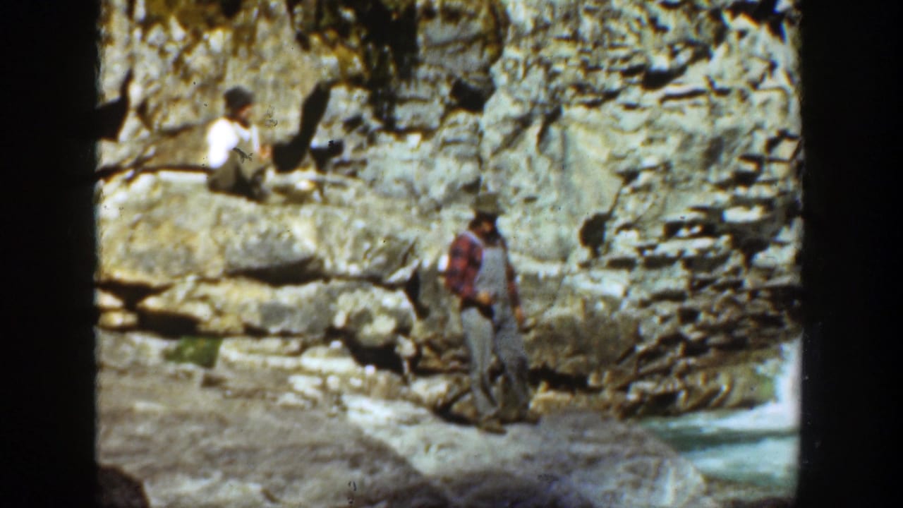 1936 California 8mm frame showing a man in a red shirt and overalls near a rocky canyon wall with another person seated above.