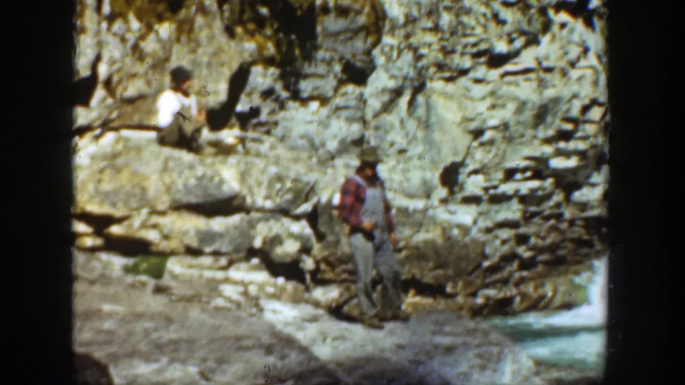 1936 California 8mm frame showing a man in a red shirt and overalls near a rocky canyon wall with another person seated above.