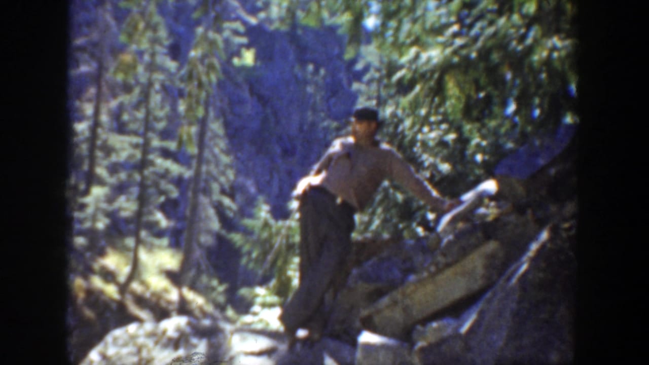 1936 California home-movie frame showing an adult man moving across rocks and fallen timber in a wooded mountain setting.