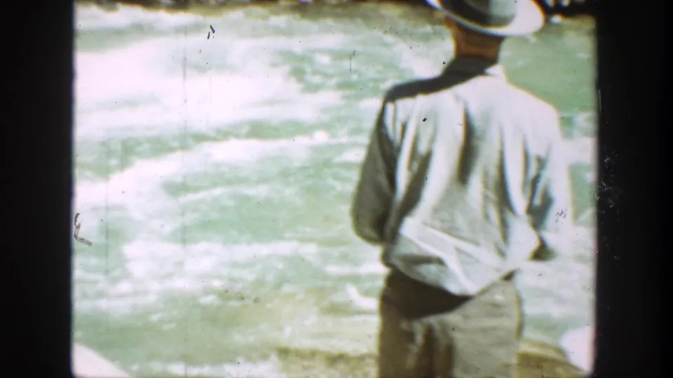 1936 California home-movie frame from behind an adult man watching or fishing near churning river water.