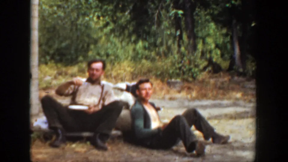 The final frame shows two adult men seated outside in California, framed by dirt ground, trees, and a rustic building edge in a 1936 home movie.