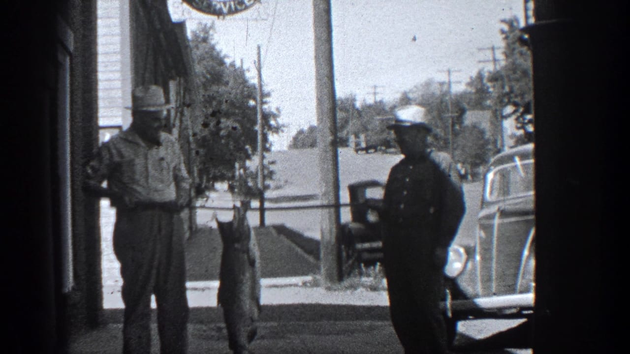 Two men stand on a shaded street beside a large fish hanging from a pole.