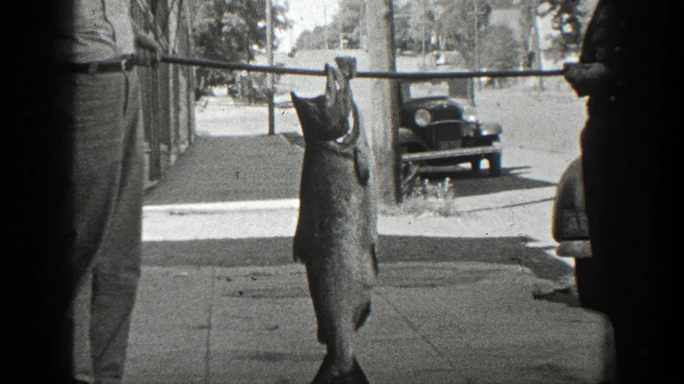 The final frame holds on the large fish suspended from a pole, with a man partly visible and a 1930s California street behind it.