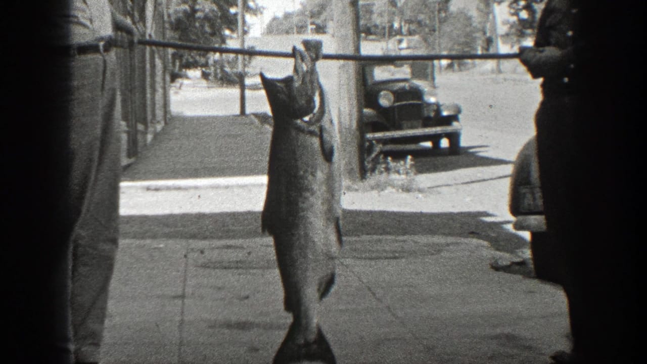 Two men hold a pole with a large fish hanging from it on a sunny street.