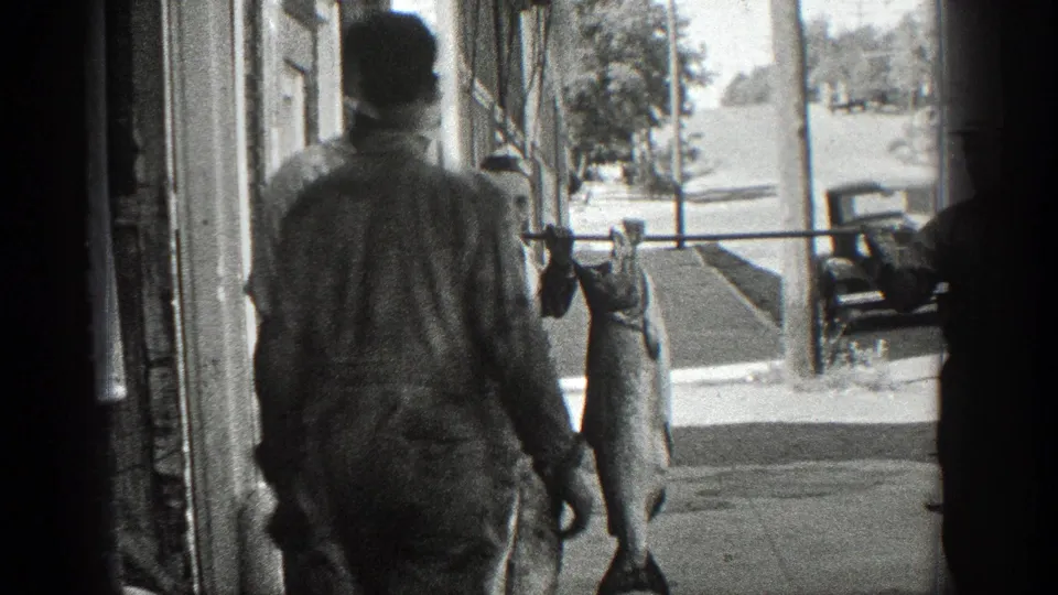 A man walks near a building frontage while the large fish remains suspended from a pole on the California street.
