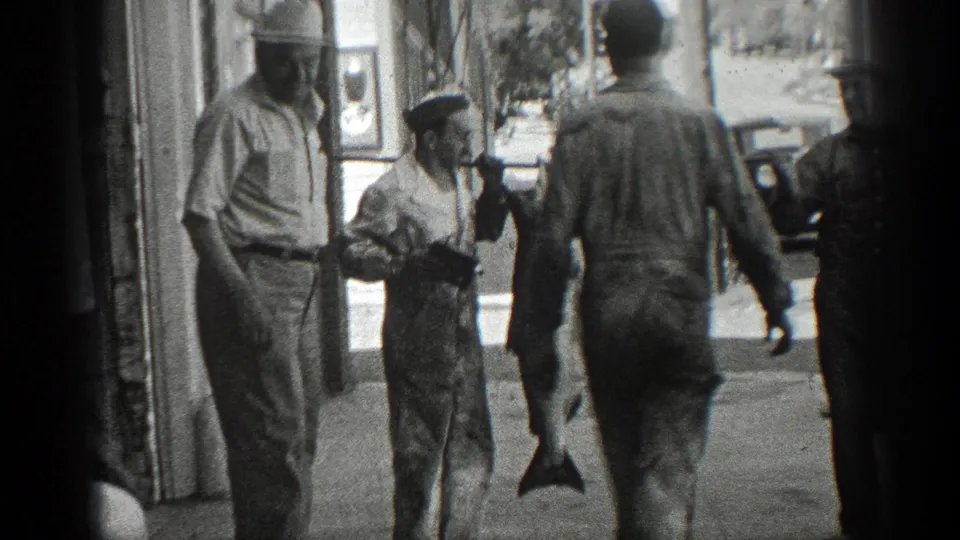 In 1936 California home-movie footage, adult men stand outside a storefront while a large fish hangs from a pole.