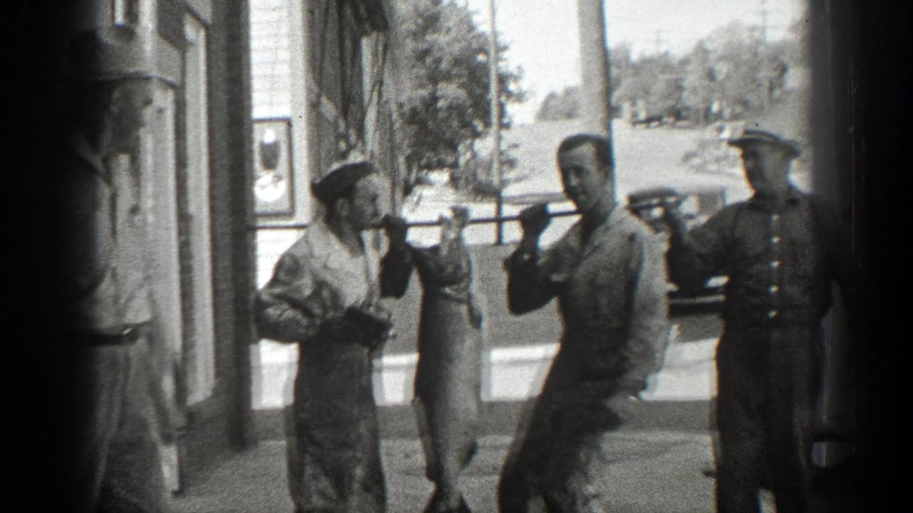 Two men hold a pole with a large fish while another man stands nearby.