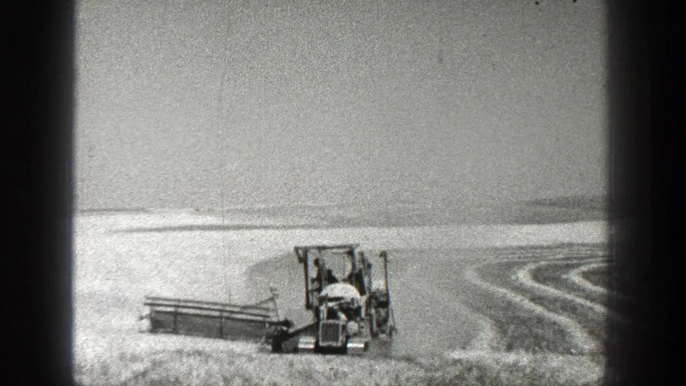 A tractor faces the camera while pulling a farm implement through a California field marked by curved rows and light-toned soil.