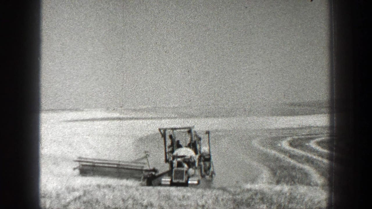 Tractor-mounted harvester moving through a wide field with curved rows behind it.