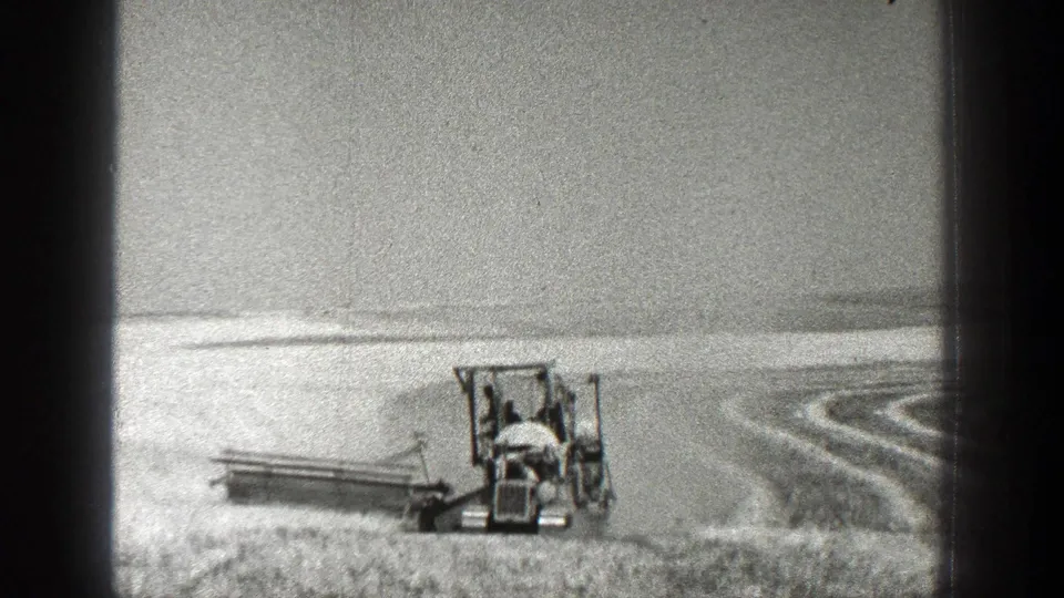 1936 California 8mm frame showing a tractor-mounted harvester working across an open field with curved rows visible in the distance.