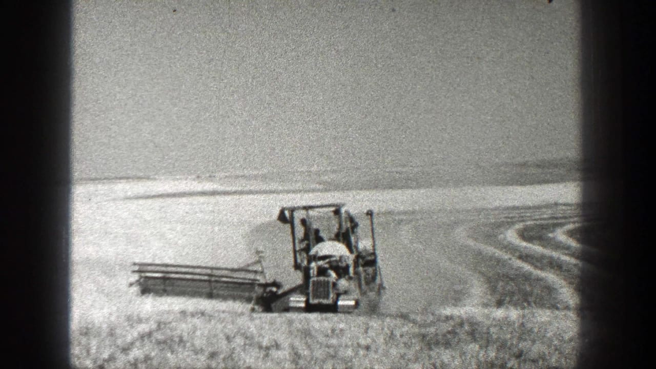 Farm machine seen front-on in a bright field with curved row marks at right.