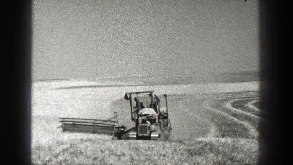 1936 California home-movie frame of a front-facing farm machine operating in a broad field with curved harvested rows nearby.