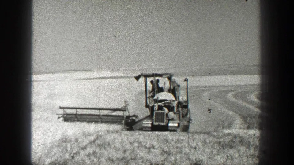 1936 California 8mm frame showing a tractor-mounted harvester with its cutting attachment extending across the field.