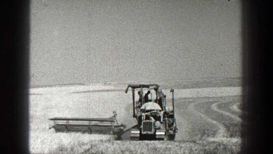 1936 California home-movie frame with a tractor harvester at right and broad field rows stretching behind it.