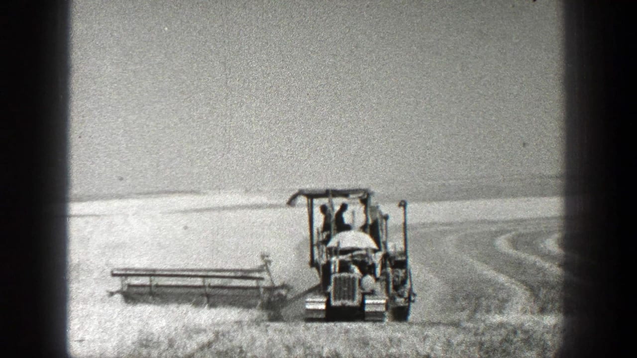 Tractor with operator moving across an open field beside a trailing farm implement.