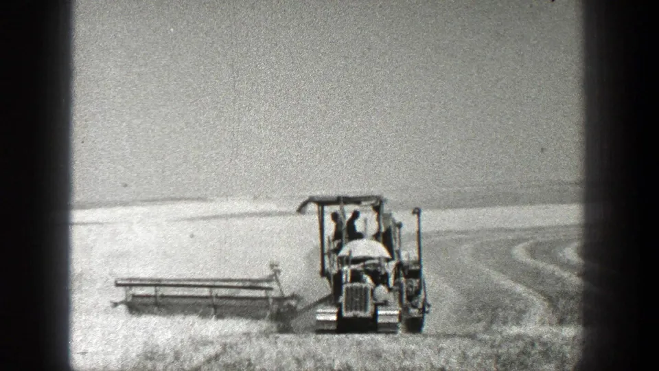 1936 California home-movie frame showing a tractor and visible operator working across a broad agricultural field.