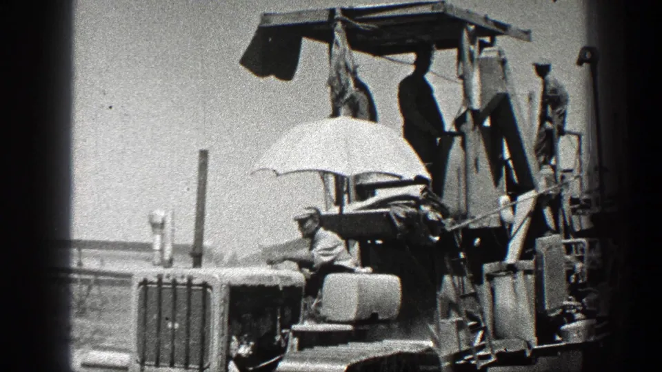 1936 California farm footage showing workers on top of a tractor or agricultural machine, with one man seated under a white umbrella.