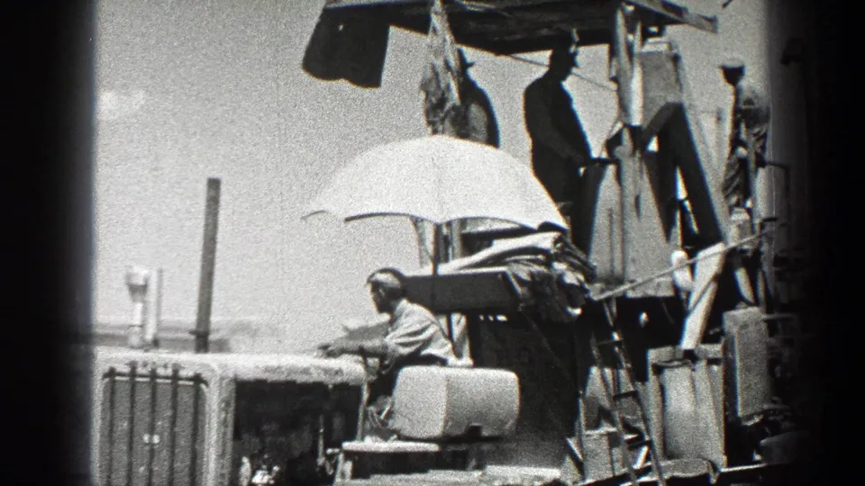Workers appear on a tractor or farm apparatus in California, with a seated operator shaded by an umbrella and others standing above him.