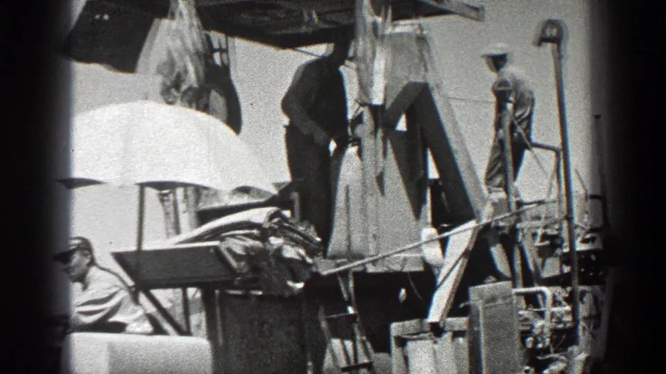 A closer 8mm frame shows workers standing on the upper part of farm machinery, with the seated operator partly cropped at lower left.