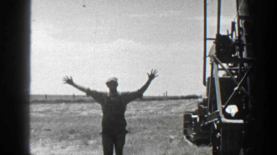 Black-and-white 8mm frame showing a man with raised arms near oil-field equipment in California, 1936.