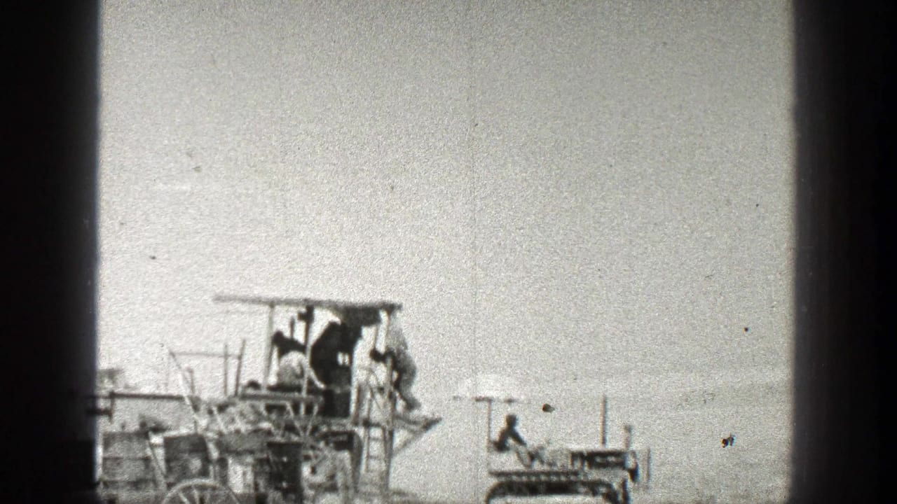 1936 California home-movie frame showing people on a wooden apparatus while a small tracked vehicle sits nearby in an open outdoor area.
