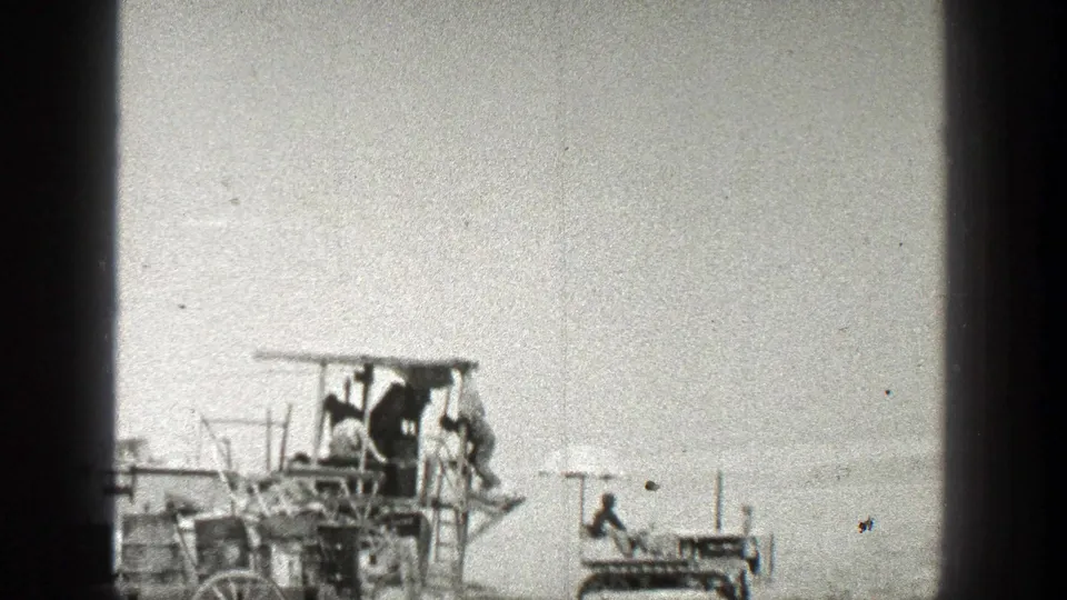 1936 California home-movie frame showing people on a wooden apparatus while a small tracked vehicle sits nearby in an open outdoor area.