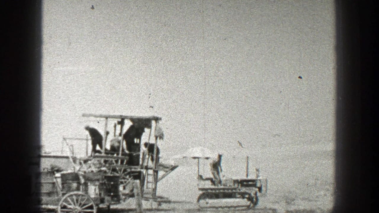 Wooden apparatus with people on it and a small tracked vehicle to the right.