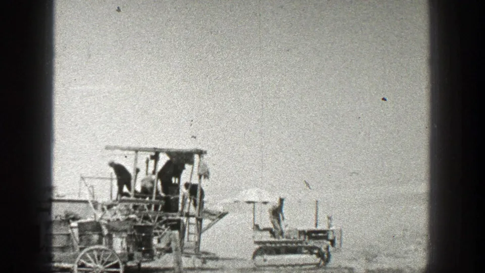 1936 California frame with several people on a wooden structure and a compact tracked vehicle positioned to the right in bright outdoor light.