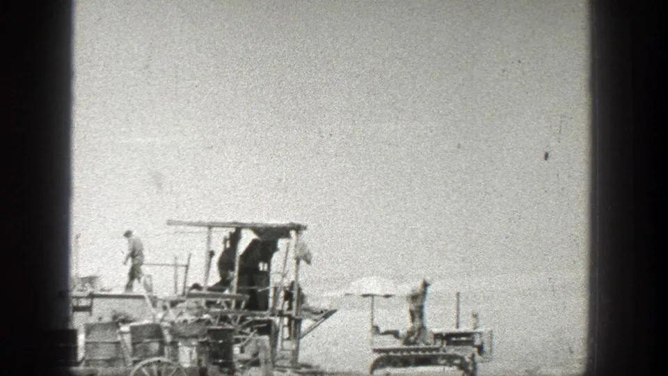 1936 California home-movie frame showing people descending from a wooden structure as another figure stands by a small tracked vehicle.