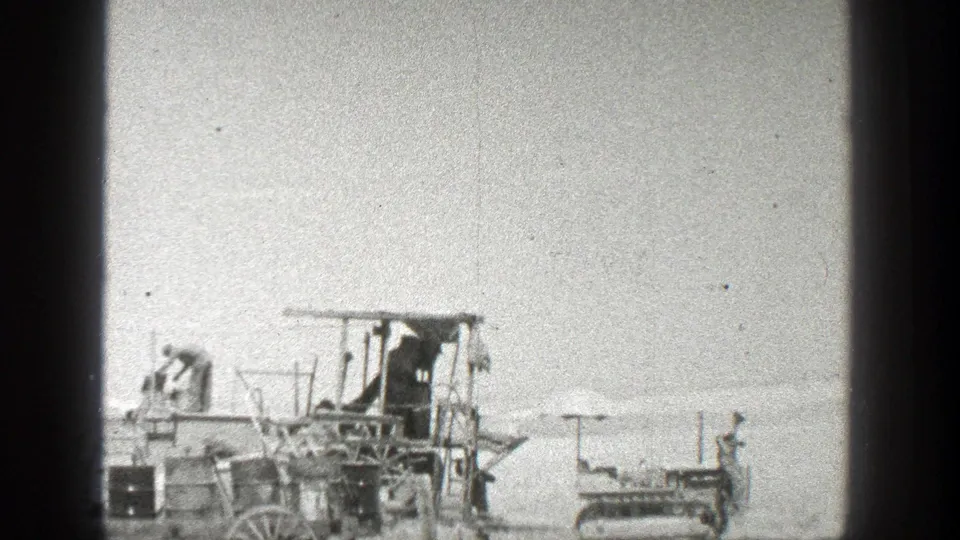 1936 California frame showing activity around a wooden apparatus, with one figure near the structure and another beside the tracked vehicle.
