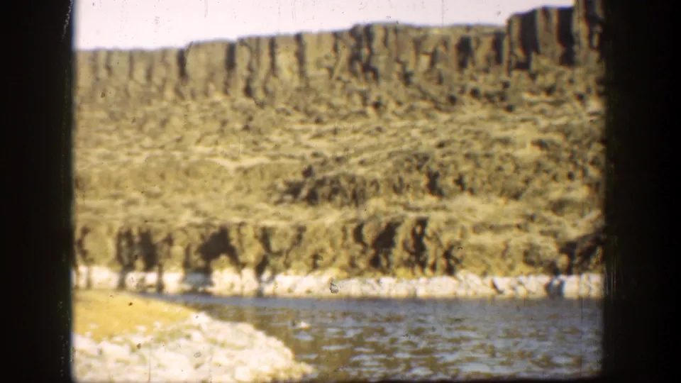 1936 California home-movie frame showing blue lake water, a rocky point, dry hills, and clear sky.