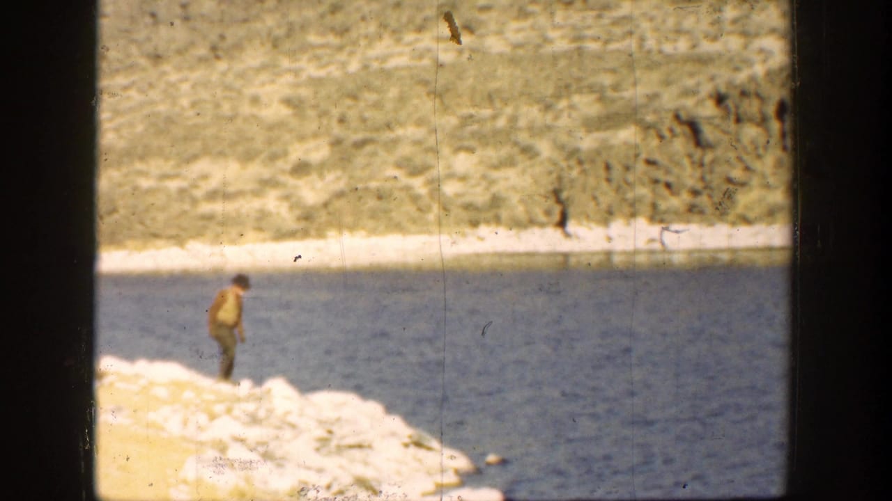Man stands on the rocky shore looking toward the river water.